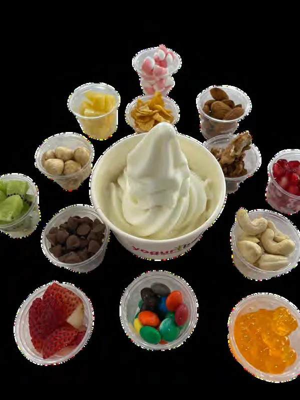 A cup of froyo surrounded by fresh fruit, nuts and topping options